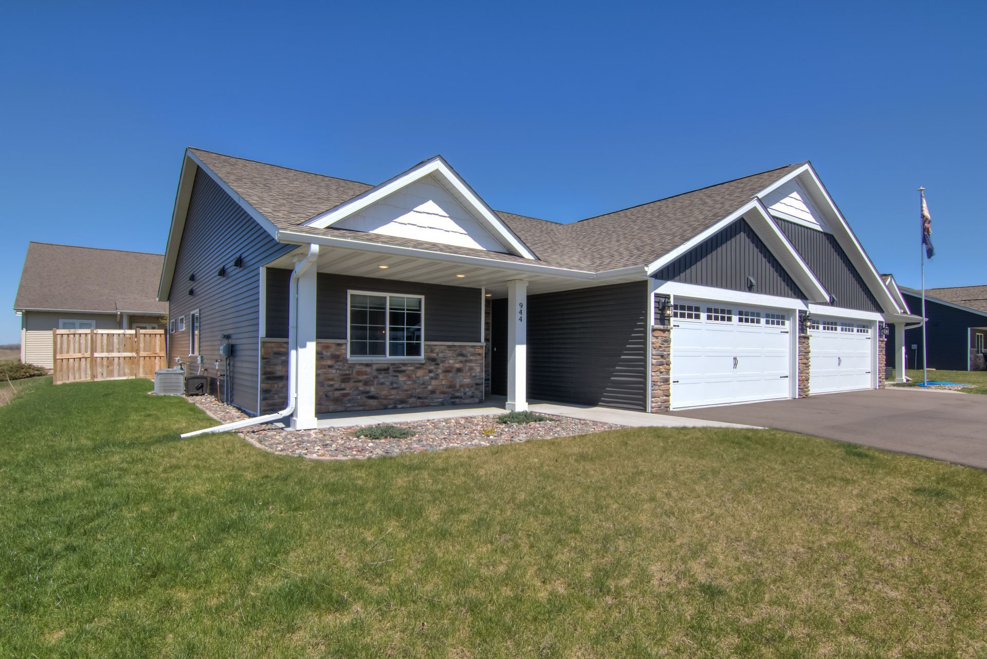 House with dark siding, white trim, and a three-car garage on a grassy lot.