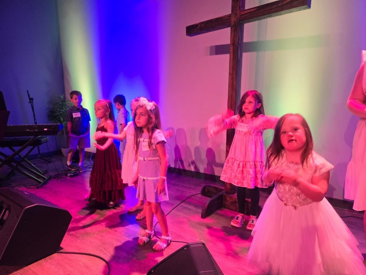 A group of young girls are dancing on a stage in front of a cross.