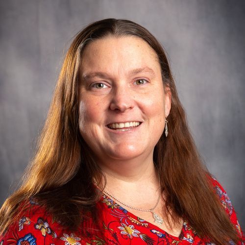 A woman in a red shirt and necklace is smiling for the camera.