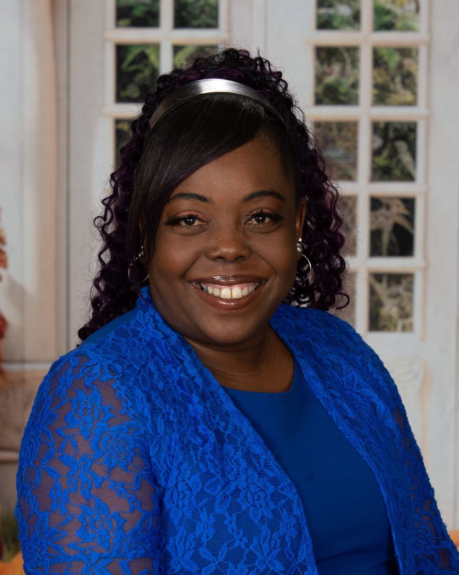 A woman wearing glasses and a blue shirt is smiling for the camera.