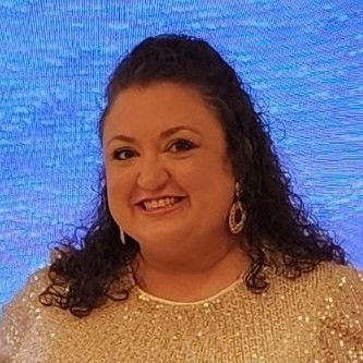 A woman wearing a gold sequined top and earrings is smiling for the camera.