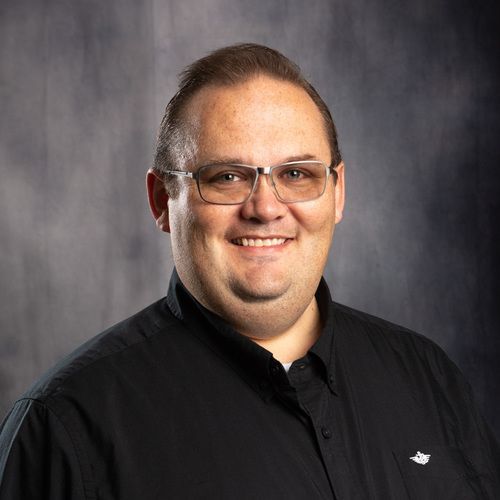 A man wearing glasses and a black shirt is smiling for the camera.