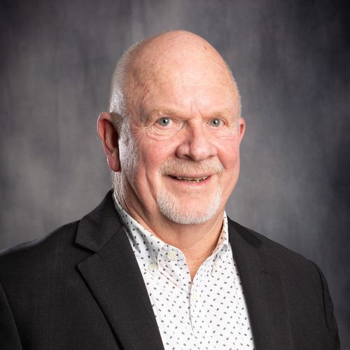 A man in a suit and polka dot shirt is smiling for the camera.