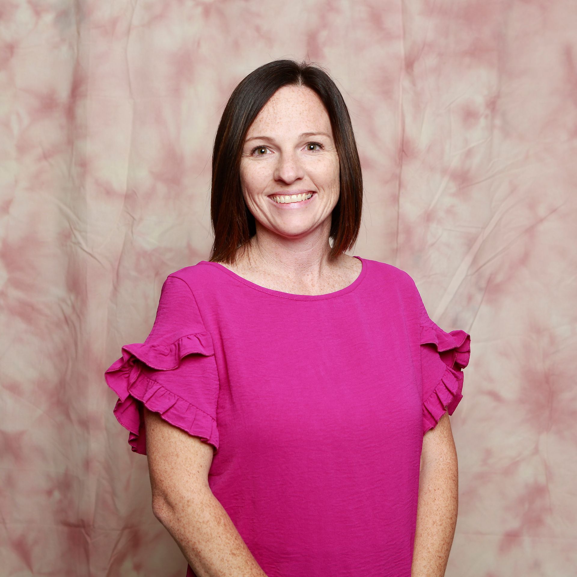A woman in a pink shirt with ruffled sleeves is smiling for the camera.