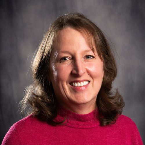 A woman in a pink sweater is smiling for the camera.
