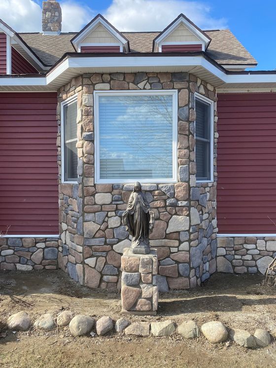 A red house with a stone wall and a statue in front of it.