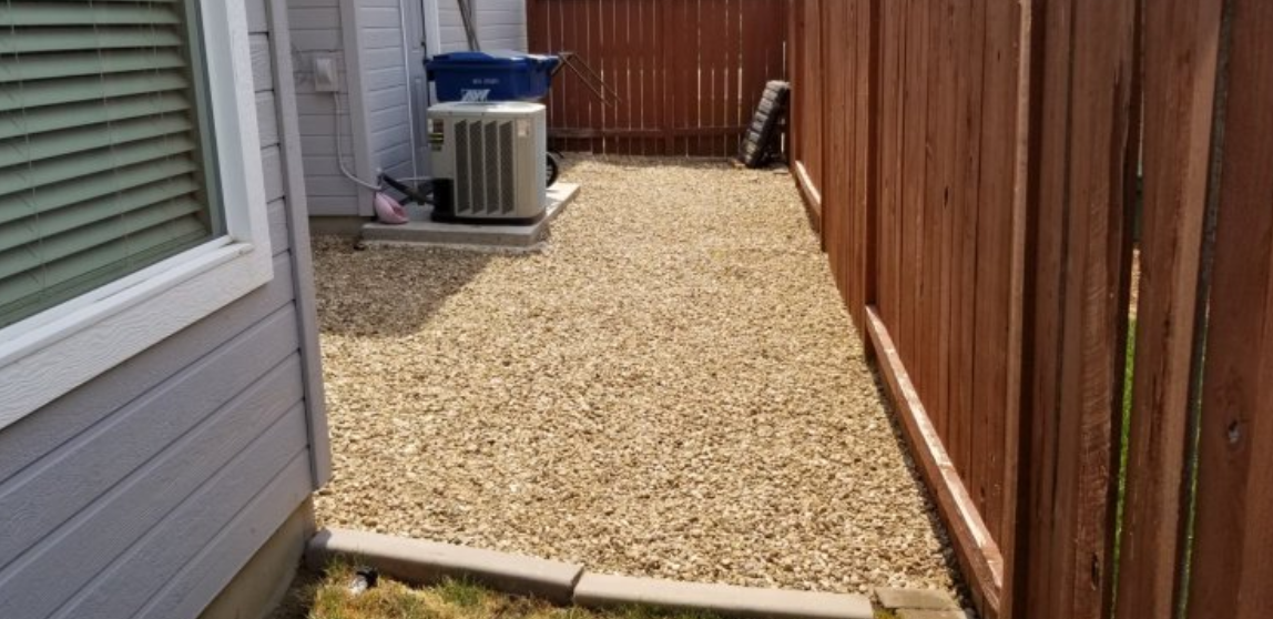 A gravel path leading to a house next to a wooden fence.