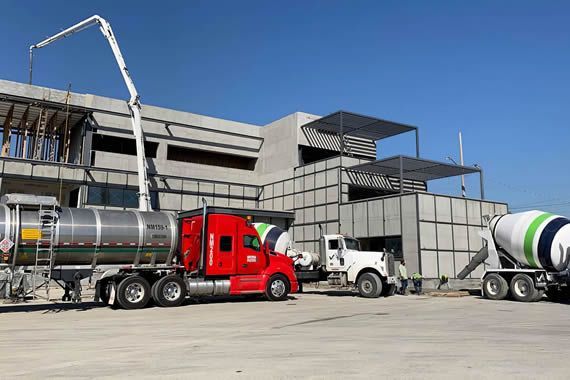 Un camión cisterna y una hormigonera están estacionados frente a un edificio en construcción.