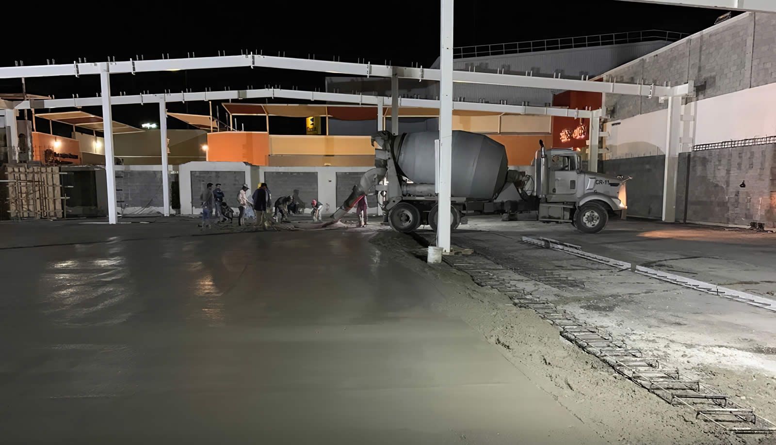 Un camión de cemento está vertiendo hormigón en un estacionamiento por la noche.
