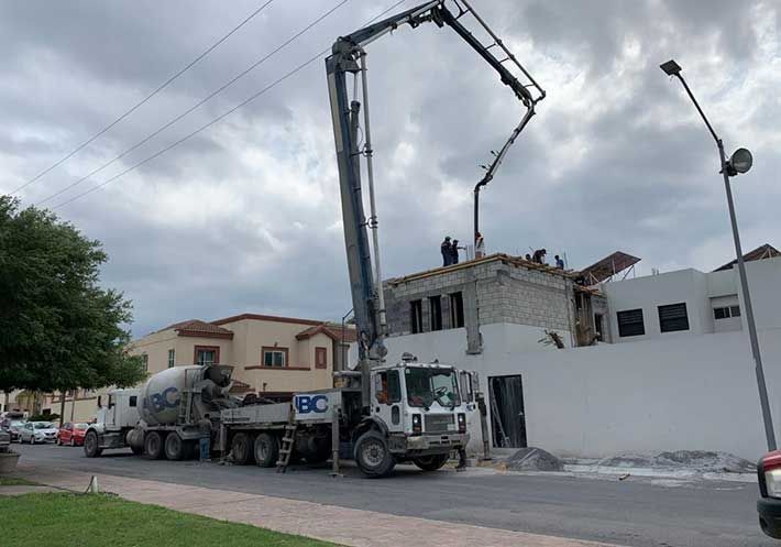 Un camión hormigonera circula por una calle frente a un edificio en construcción.