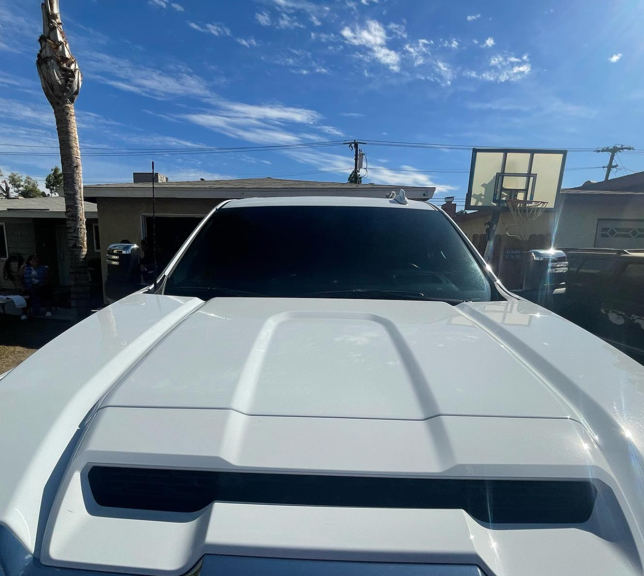 A white car with a hood scoop is parked in front of a house