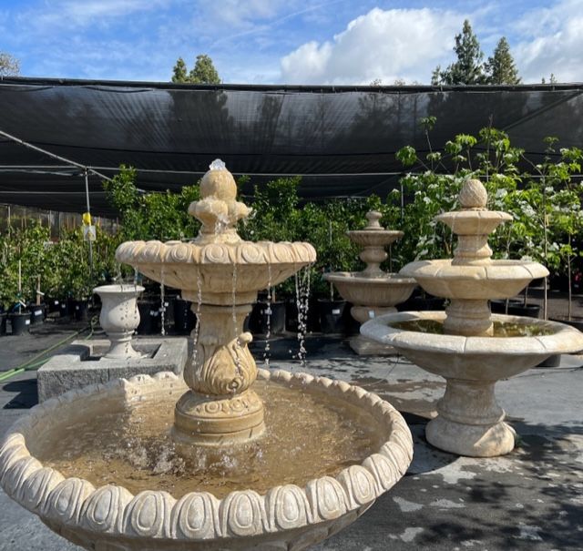 Stone fountains with water spouts, displayed outdoors under a shade cloth.