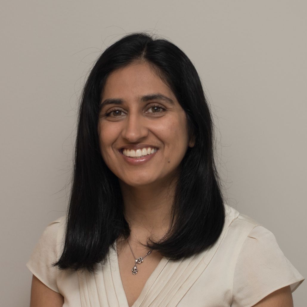A woman wearing a white shirt and a necklace smiles for the camera