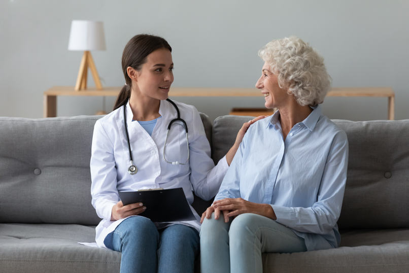 shutterstock_1619866681 A doctor is talking to an elderly woman while sitting on a couch.