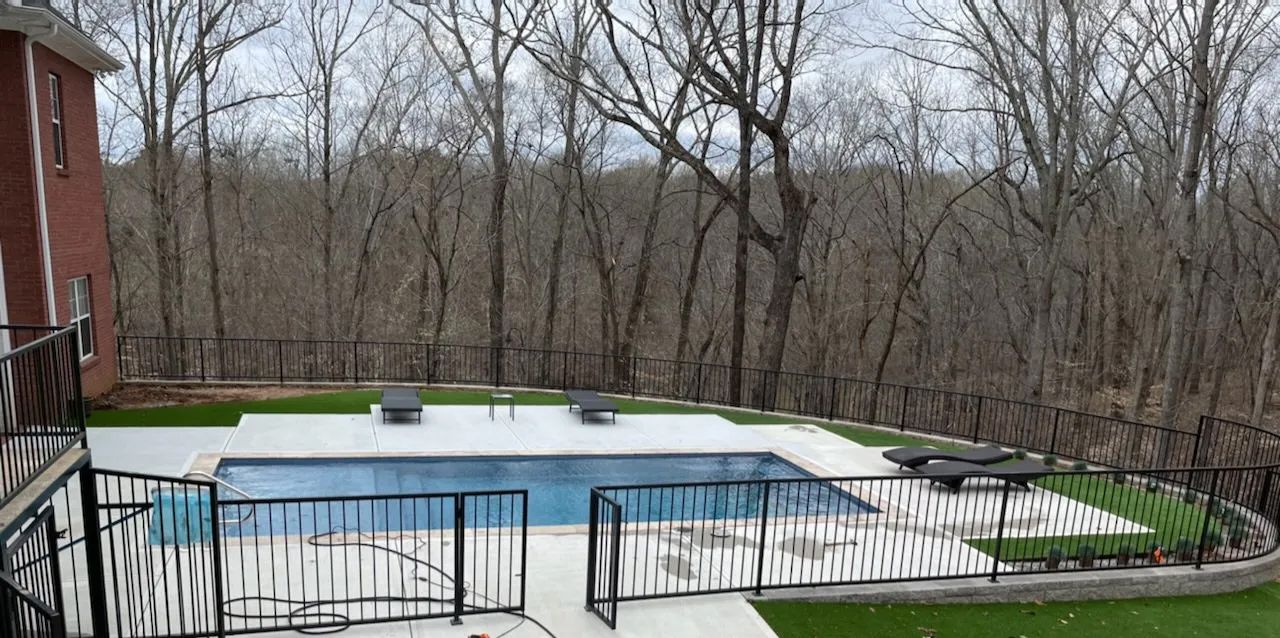 There is a large swimming pool in the backyard of a house surrounded by trees.