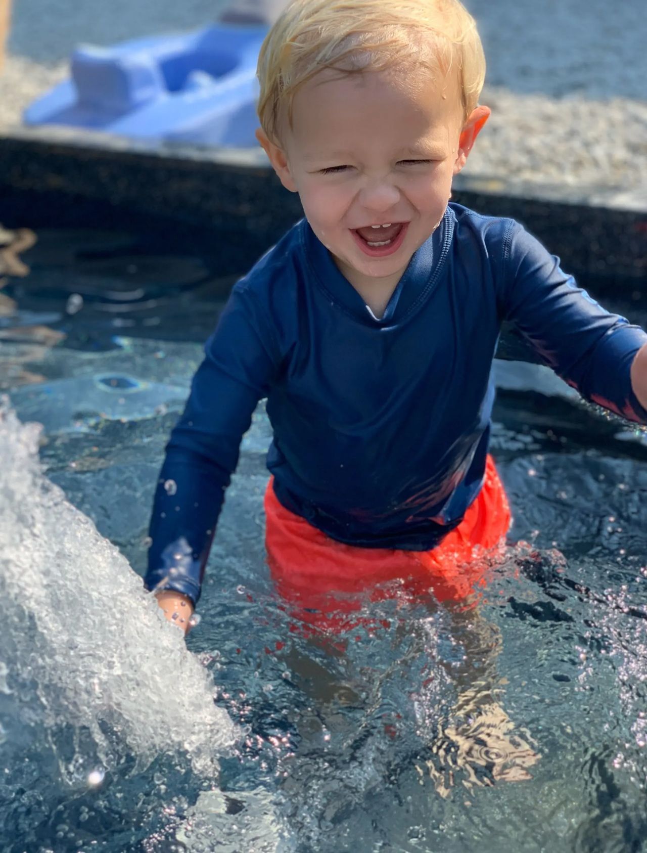 A little boy is playing in a pool of water.
