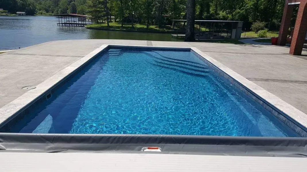 A large swimming pool is sitting next to a lake.