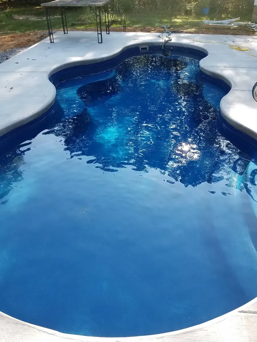A large blue swimming pool with a table and chairs in the background.