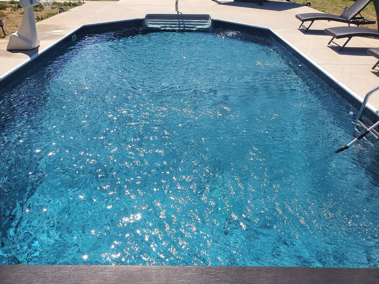 A large swimming pool filled with blue water is sitting on top of a concrete deck.