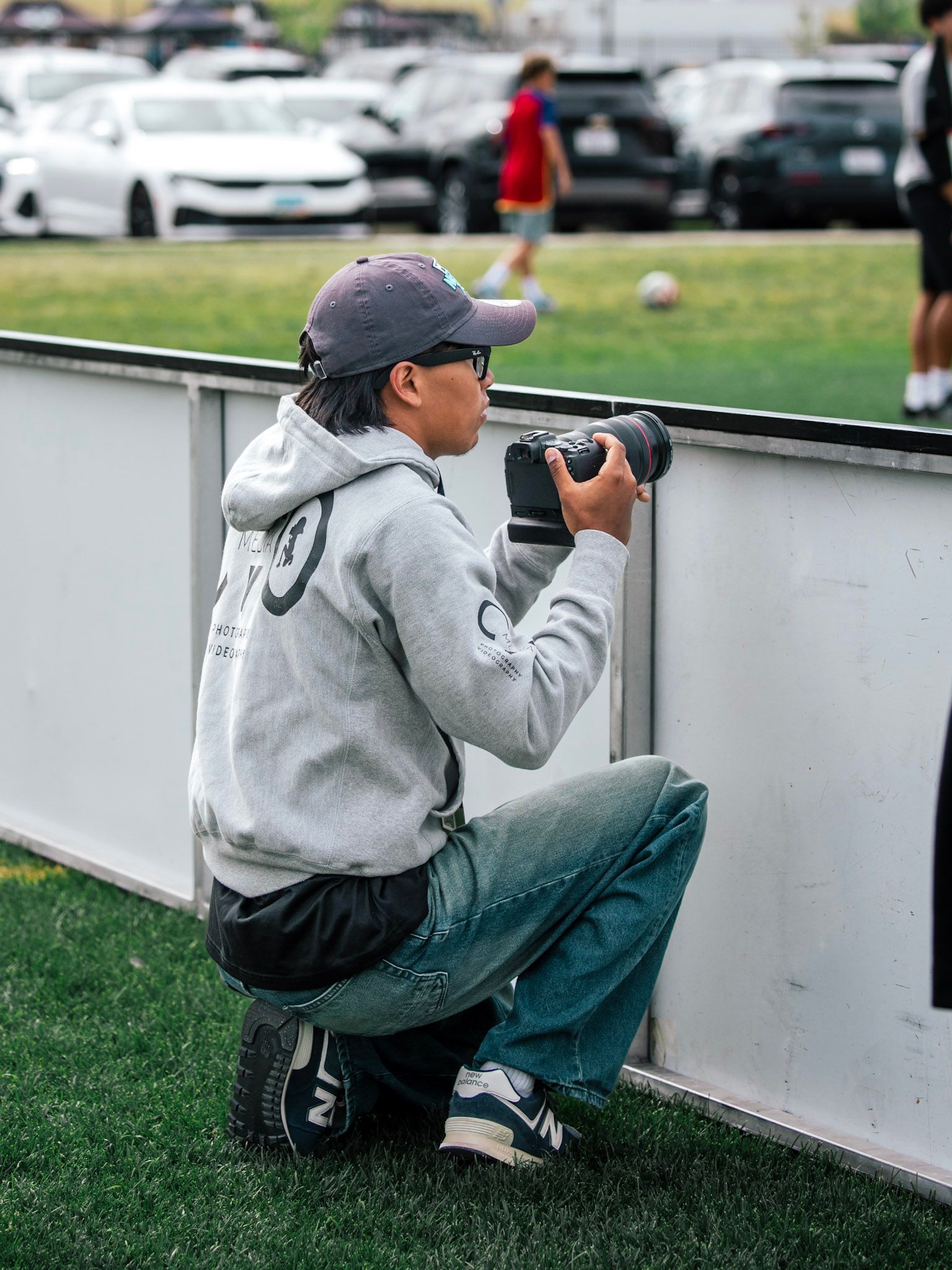Several people sit behind a chain-link fence, one holding a professional camera with a large lens.