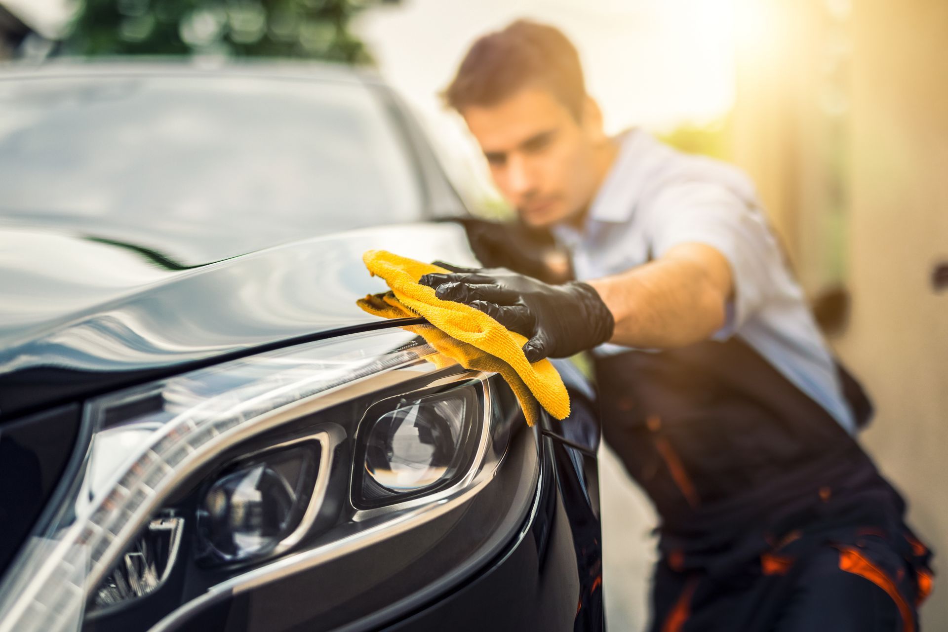 A man is cleaning a car with a yellow cloth.