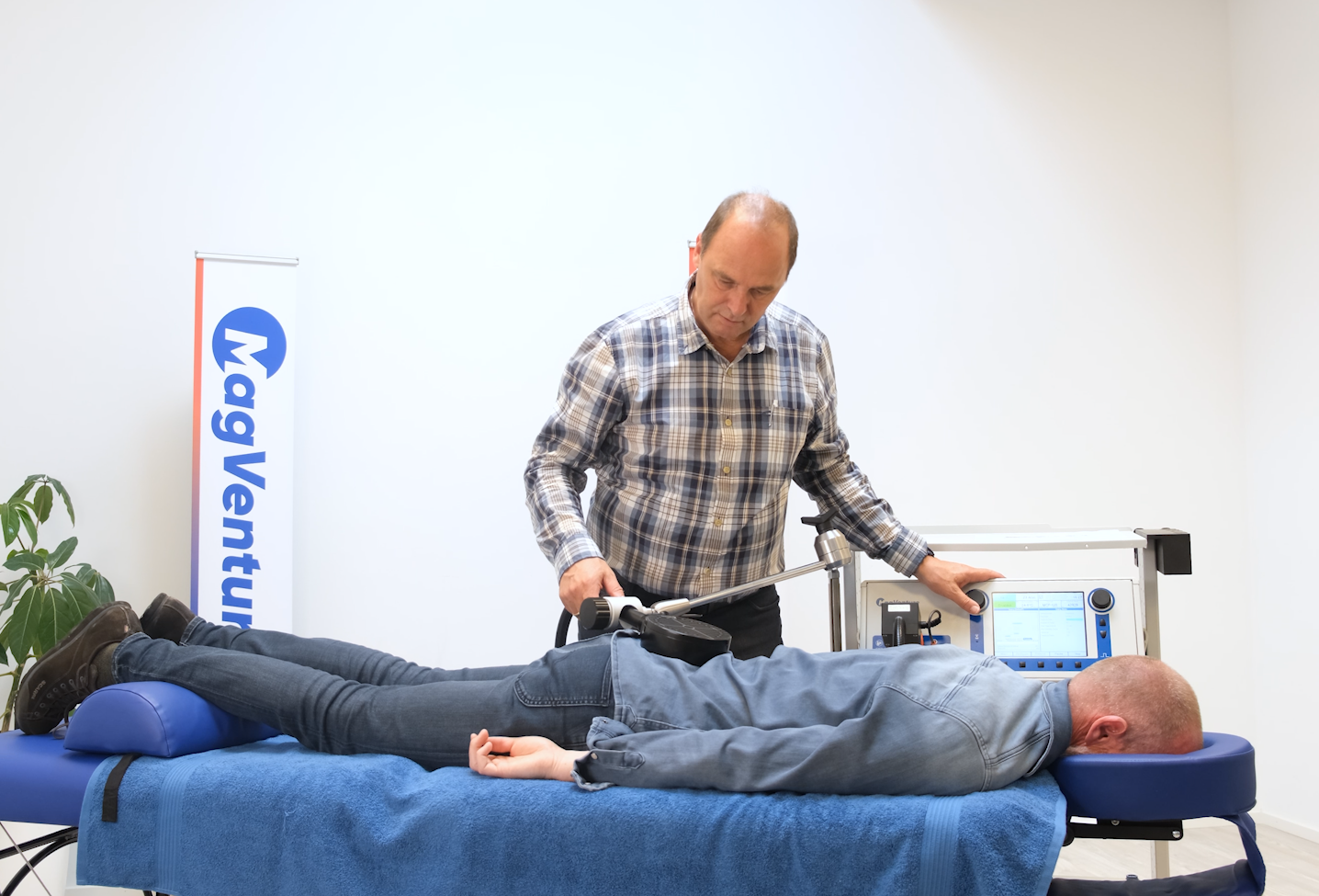 Man using a medical device on a patient lying prone on a blue table;
