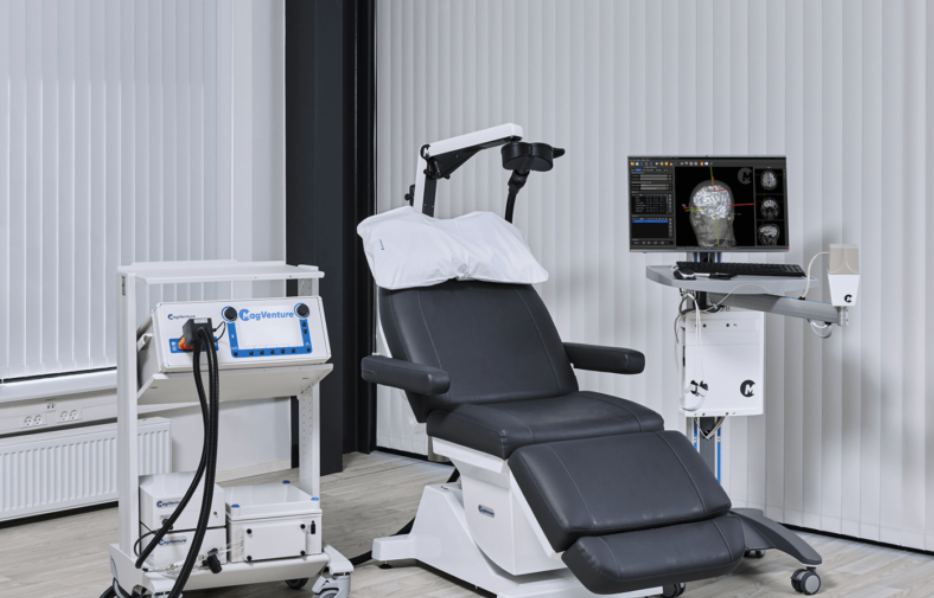 Medical device with patient chair, screen showing brain scan, and supporting equipment in a clinical setting.