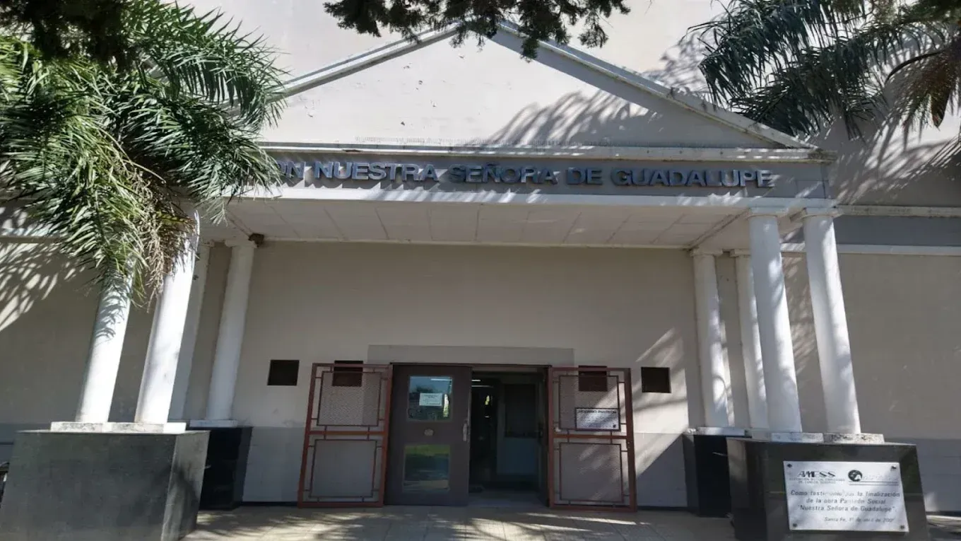 Entrada de edificio blanco con columnas y cartel sobre las puertas.