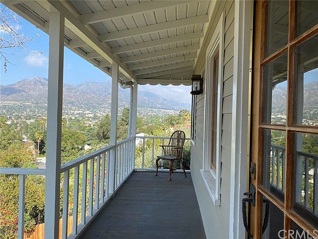 A porch with a mountain view. A chair sits on the wooden floor. White railings and beams.
