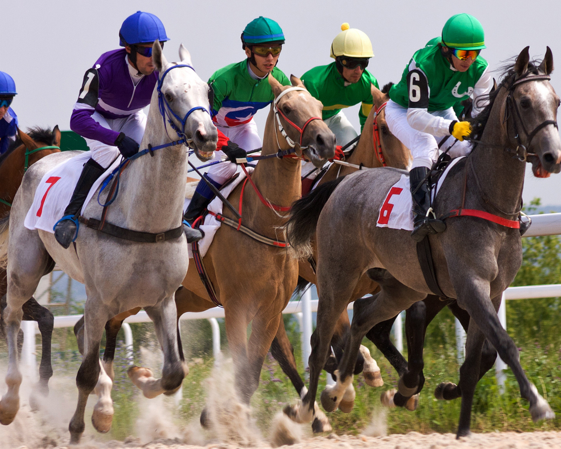 Horses and jockeys racing on a dirt track; jockeys wear colorful helmets and riding attire, some dust in the air.