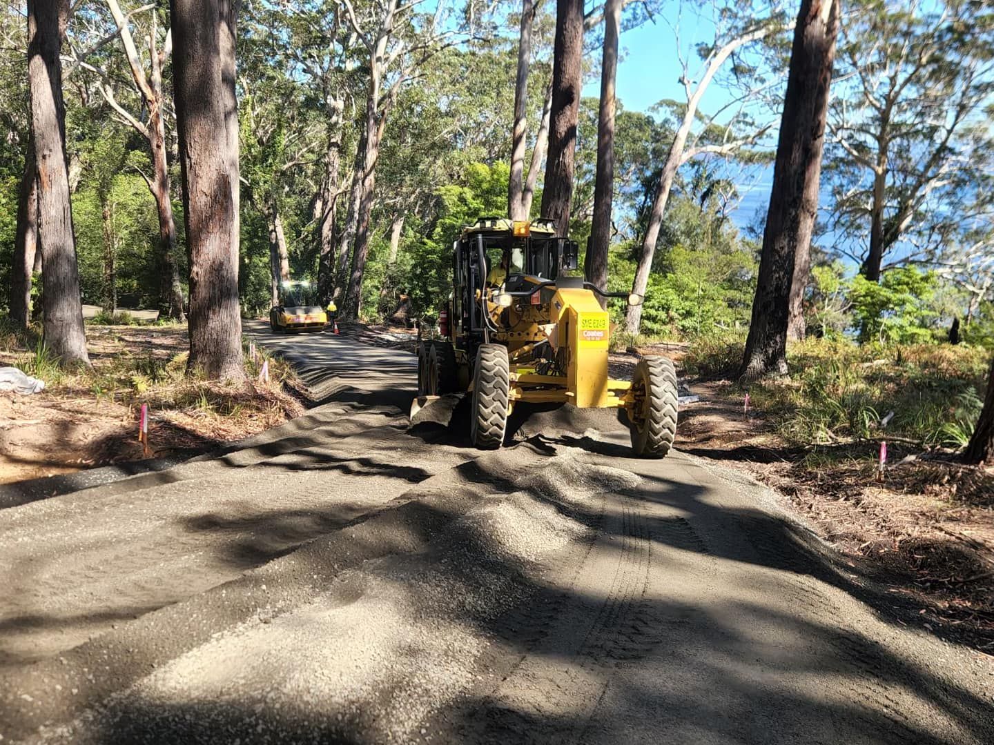 A Yellow Grader Levels a Gravel Road in a Forest, and Trees — ALI Civil Pty Ltd in South Nowra, NSW