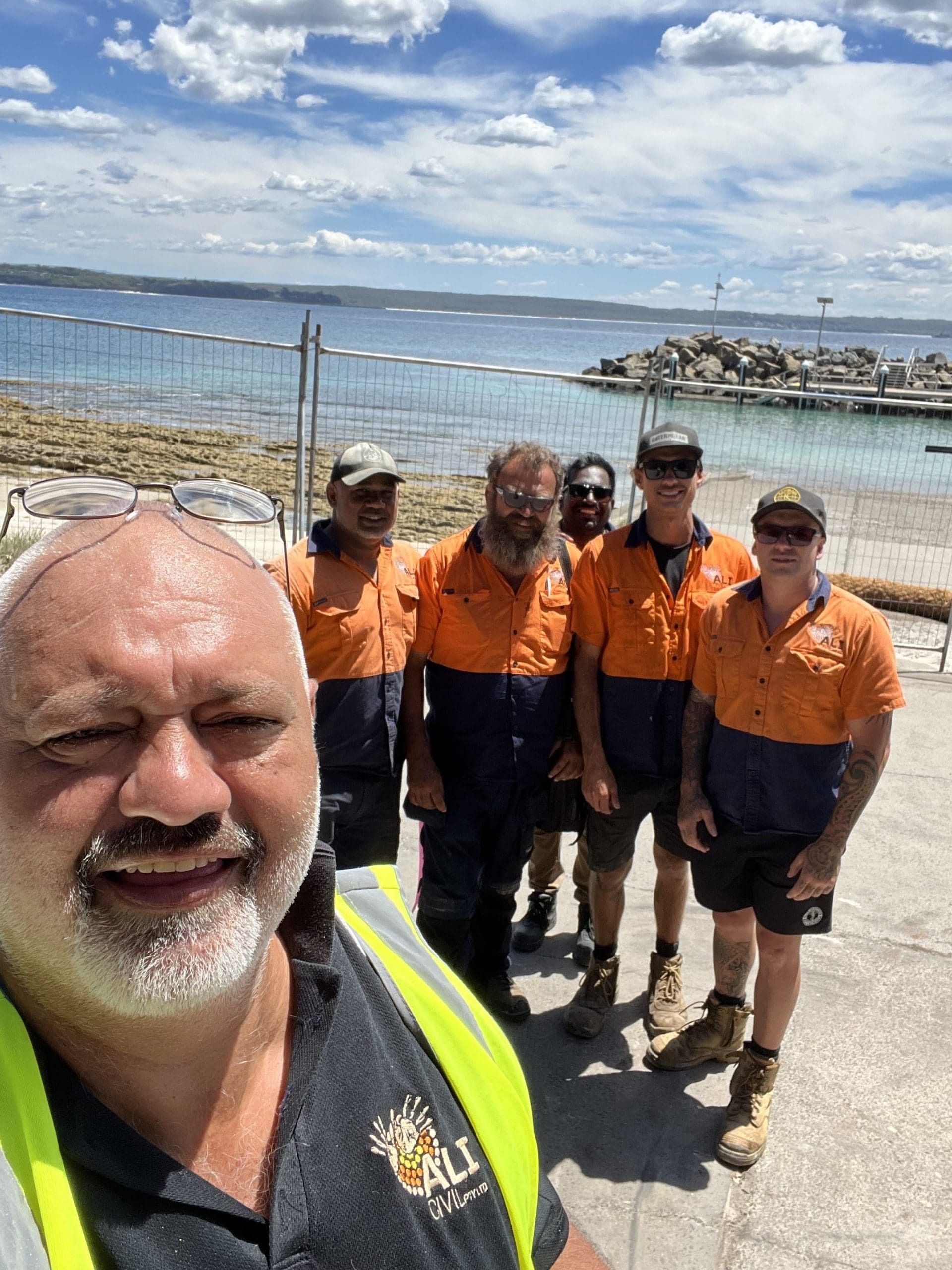 Group of construction workers taking a selfie by the ocean. They wear work clothes and the sky is bright. — ALI Civil Pty Ltd in South Nowra, NSW