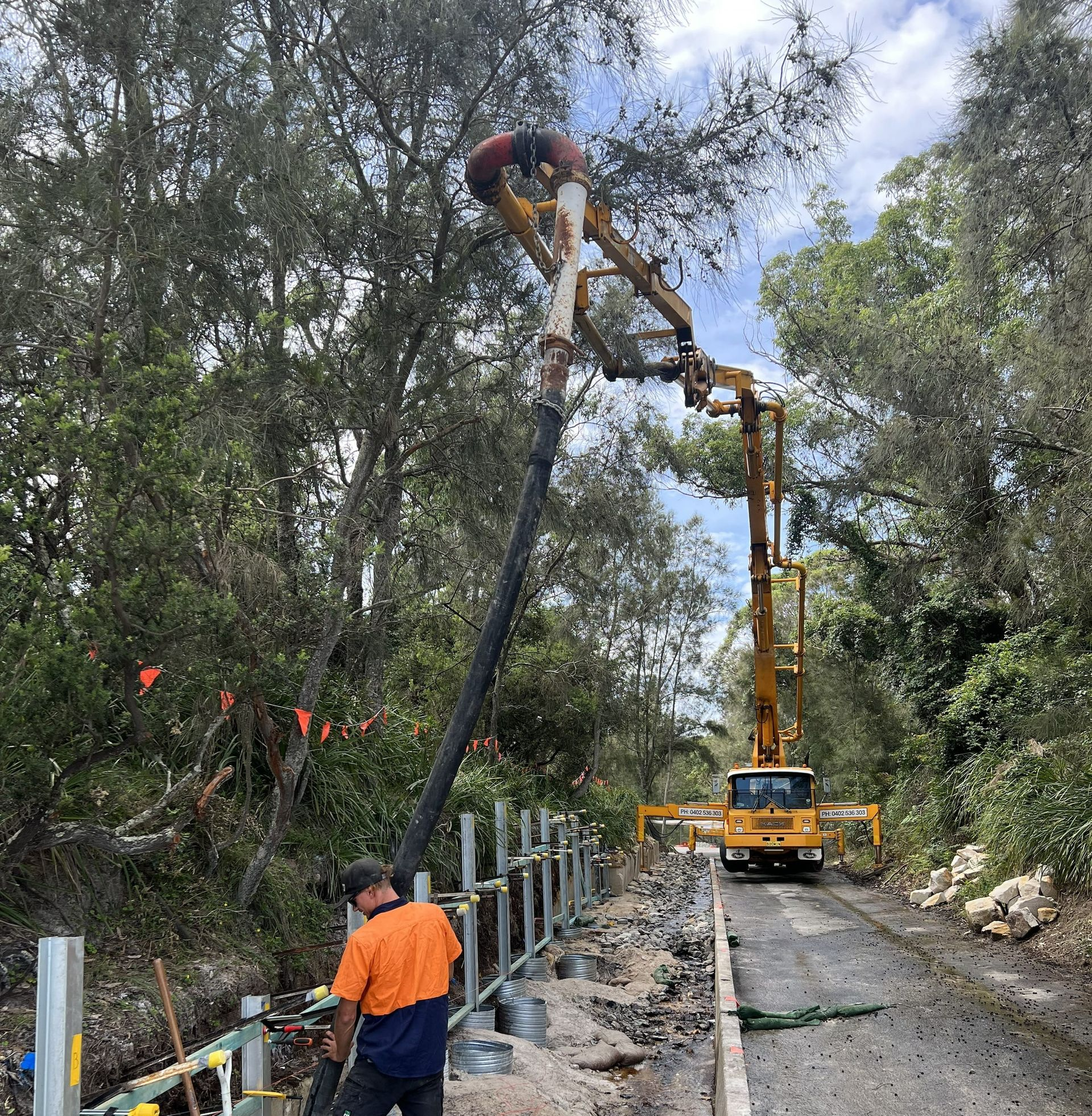 Construction workers using a concrete pump to pour concrete.  A road is being built along a tree lined pathway. — ALI Civil Pty Ltd in South Nowra, NSW