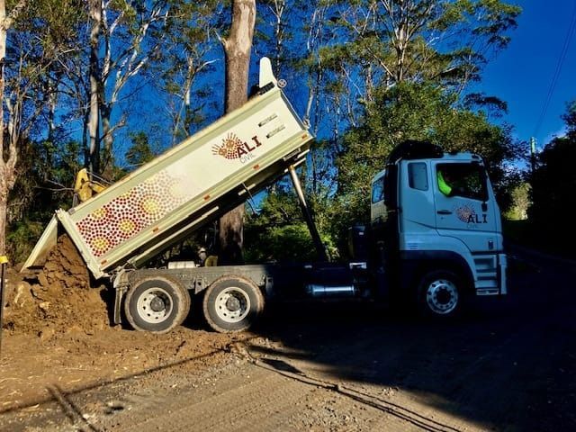 Dump truck dumping dirt on a dirt road, trees in the background. — ALI Civil Pty Ltd in South Nowra, NSW