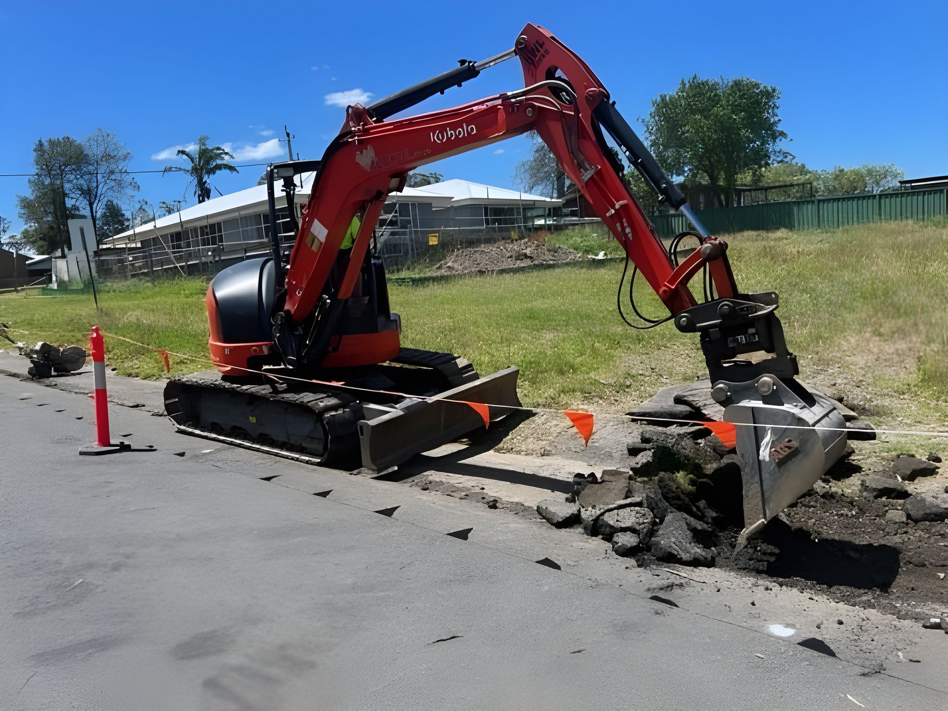 Mini excavator removing asphalt from a roadside curb on a sunny day. — ALI Civil Pty Ltd in South Nowra, NSW