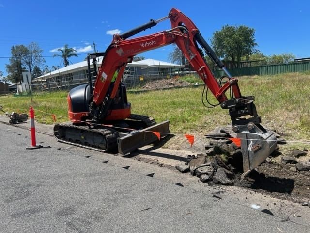 Red Kubota excavator demolishing asphalt curb on a sunny day. — ALI Civil Pty Ltd in South Nowra, NSW
