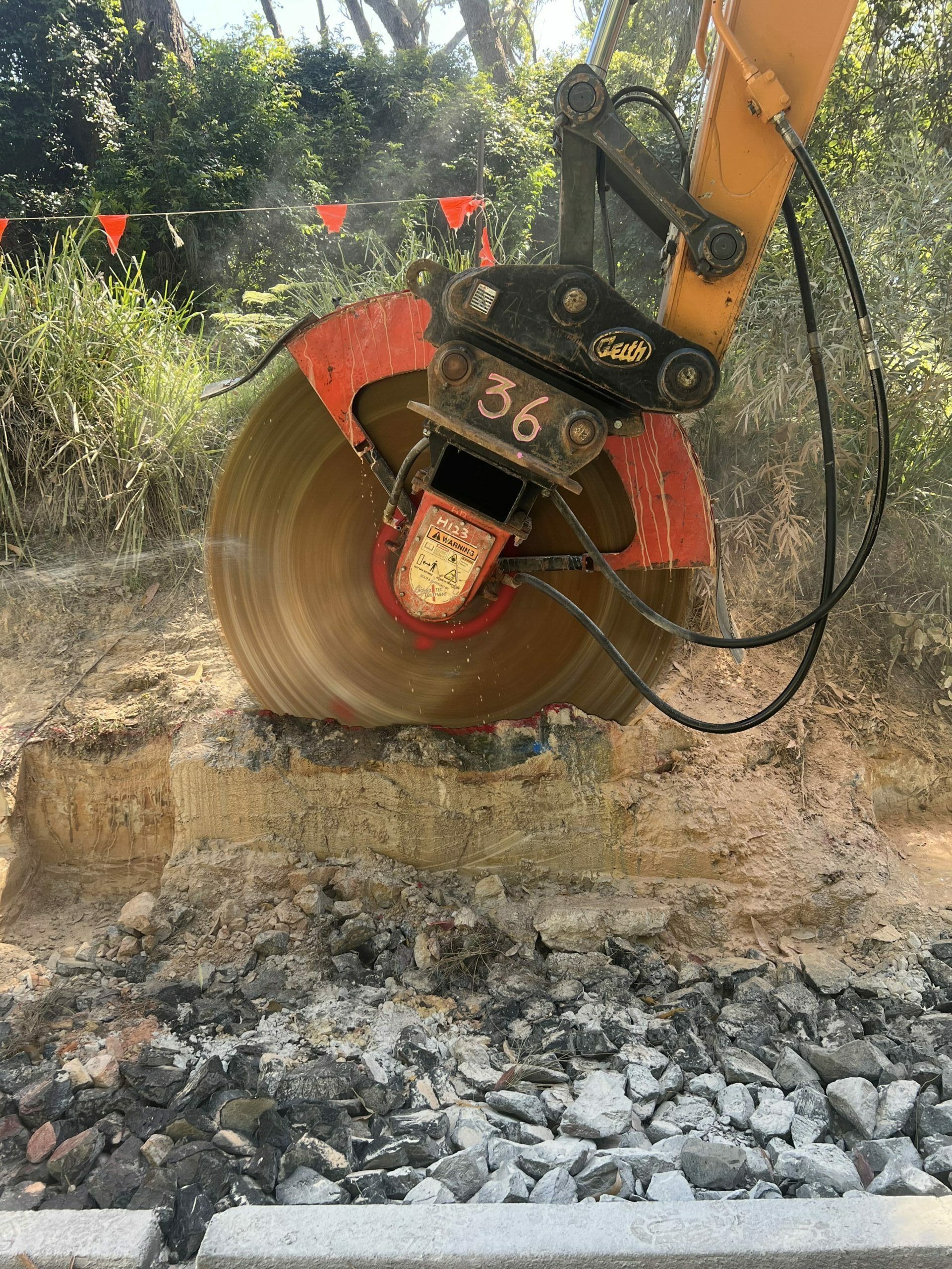 Excavator with a circular saw cutting through a dirt and rock-filled trench in an outdoor setting. — ALI Civil Pty Ltd in South Nowra, NSW