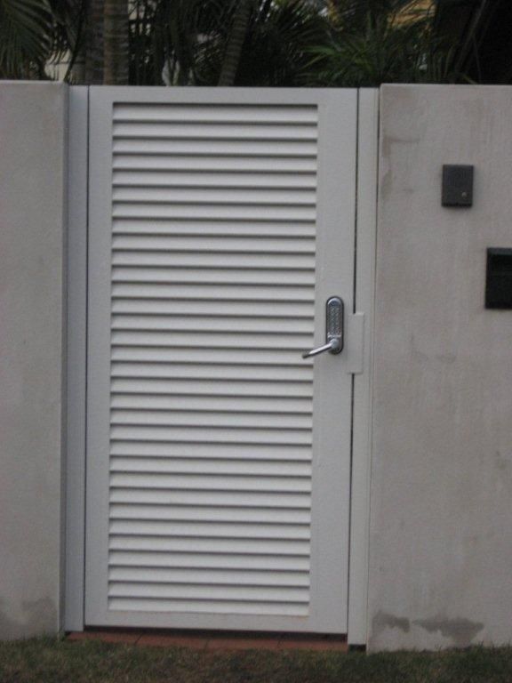 A White Aluminium Gate With Shutters On It Is In Front Of A Concrete Wall — AAA Fencing & Supplies in Southport, QLD