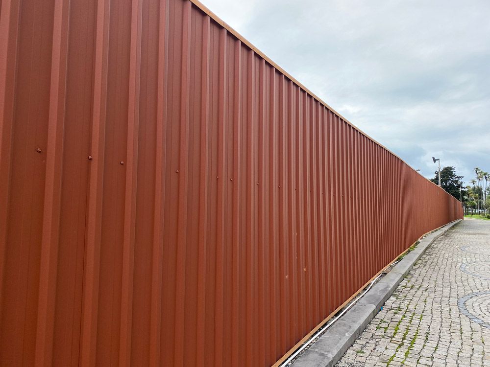 A Long Red Metal Fence Along A Cobblestone Street — AAA Fencing & Supplies in Southport, QLD