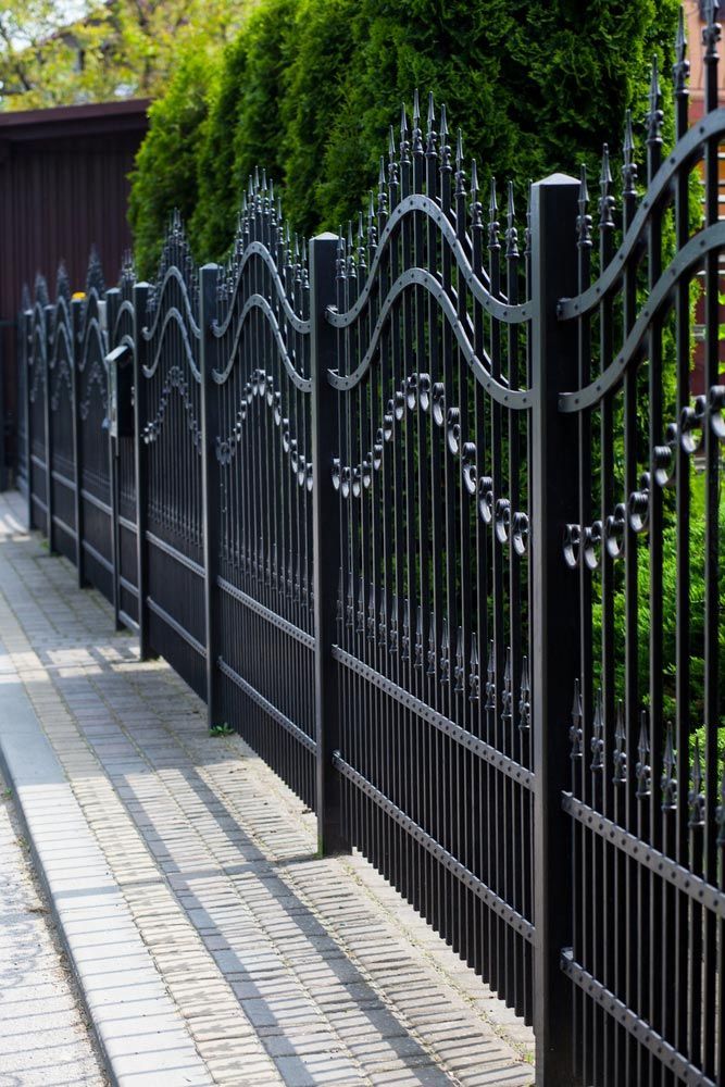 A Black Wrought Iron Fence Along A Sidewalk With Trees In The Background — AAA Fencing & Supplies in Southport, QLD