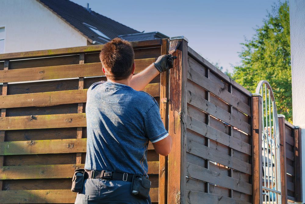A Man Is Standing Next To A Wooden Fence — AAA Fencing & Supplies in Southport, QLD