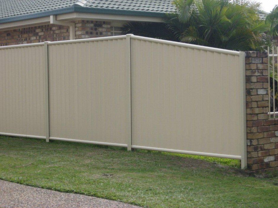 A White Colorbond Fence Is Surrounding A Brick Wall In Front Of A House — AAA Fencing & Supplies in Southport, QLD