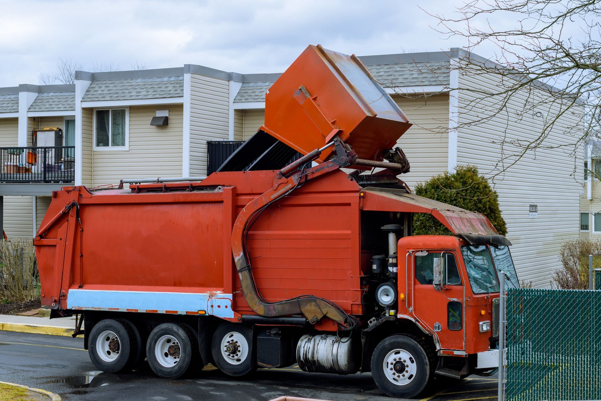 Red garbage truck with raised container in front of a building.
