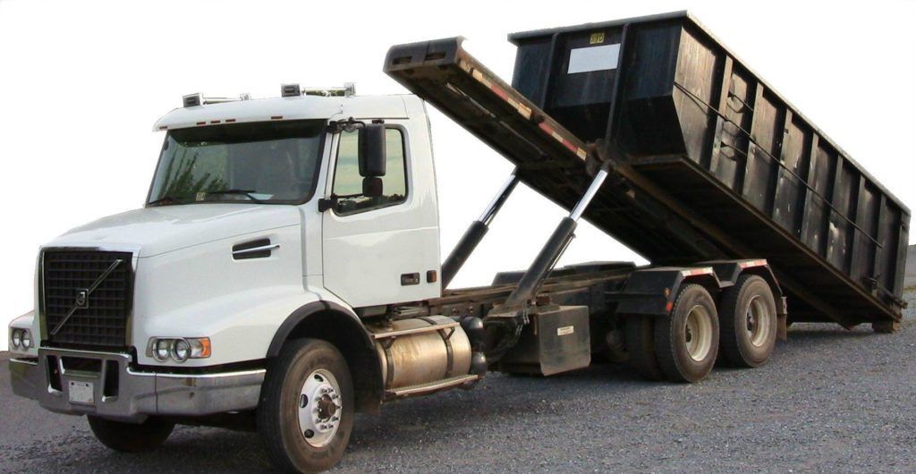 Orange dumpster on wheels, parked on asphalt with safety cones.