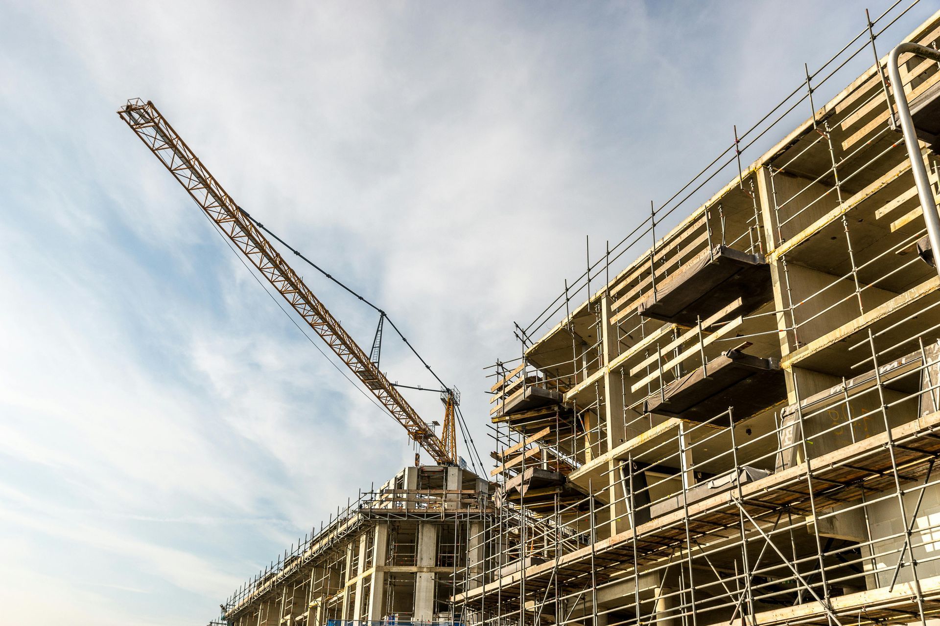 A large tower crane looms over the concrete frame of a building under construction, surrounded by extensive scaffolding.
