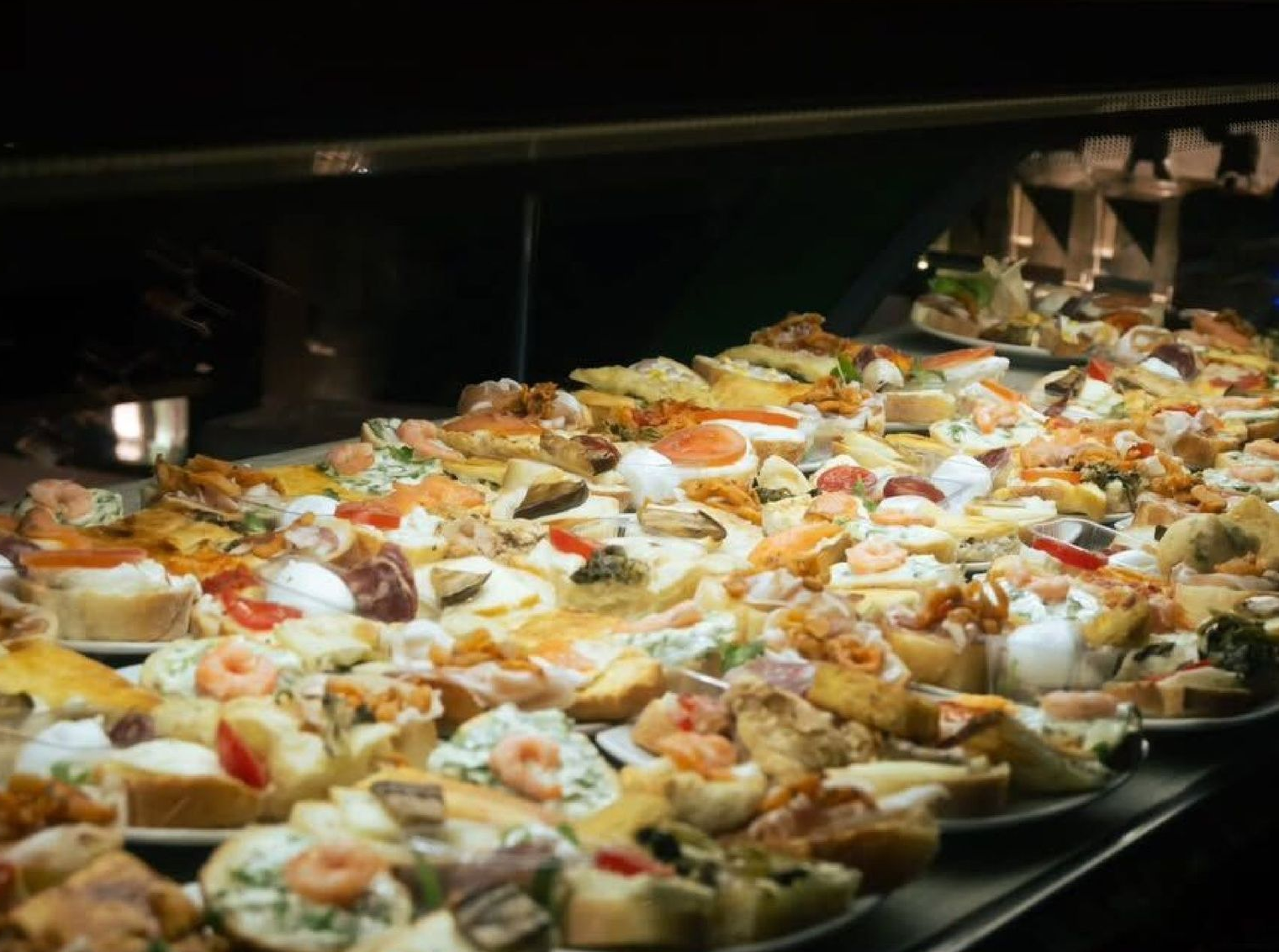 Esposizione di vari piccoli e colorati stuzzichini o tapas su piatti in un ambiente da ristorante.