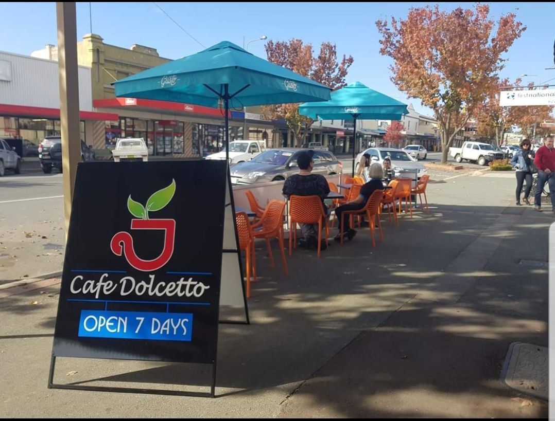 Cafe Dolcetto storefront with outdoor seating. Turquoise umbrellas, orange chairs, sign reads 