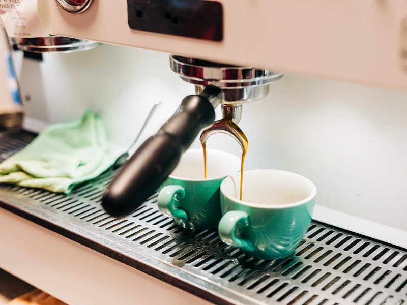 Espresso machine dispensing coffee into two teal mugs.
