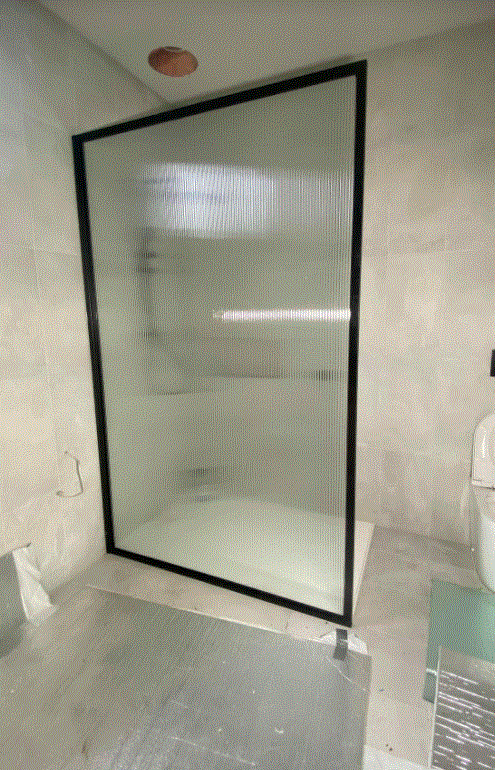 Shower with a black-framed textured glass door in a gray-tiled bathroom.