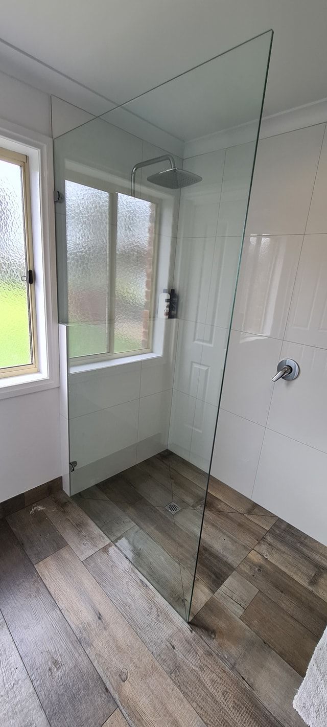 A bathroom with a walk in shower and a window.